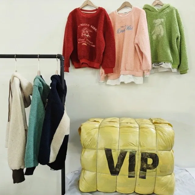 Sweaters in red, pink, green, and blue colors hanging on hangers with a yellow VIP labeled bale bag below.