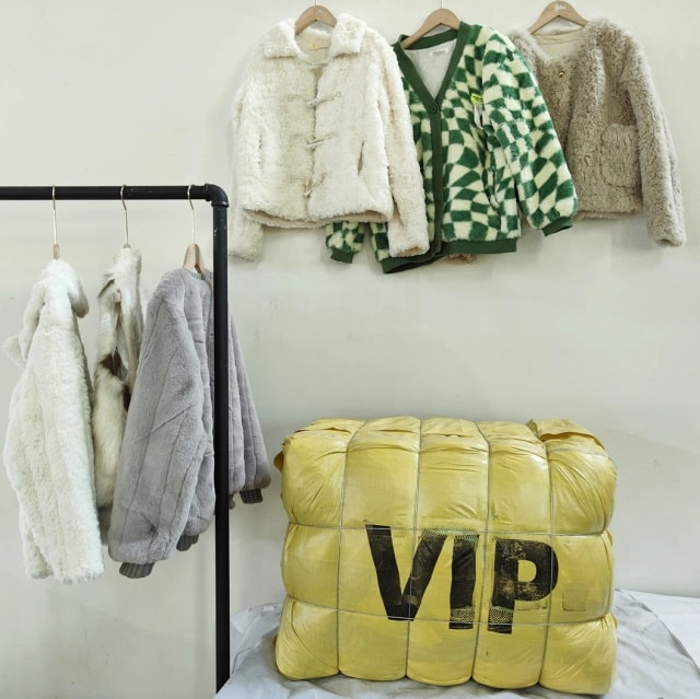 Winter jackets in white, gray, green, and beige colors displayed on hangers with a yellow VIP labeled bale in the background.