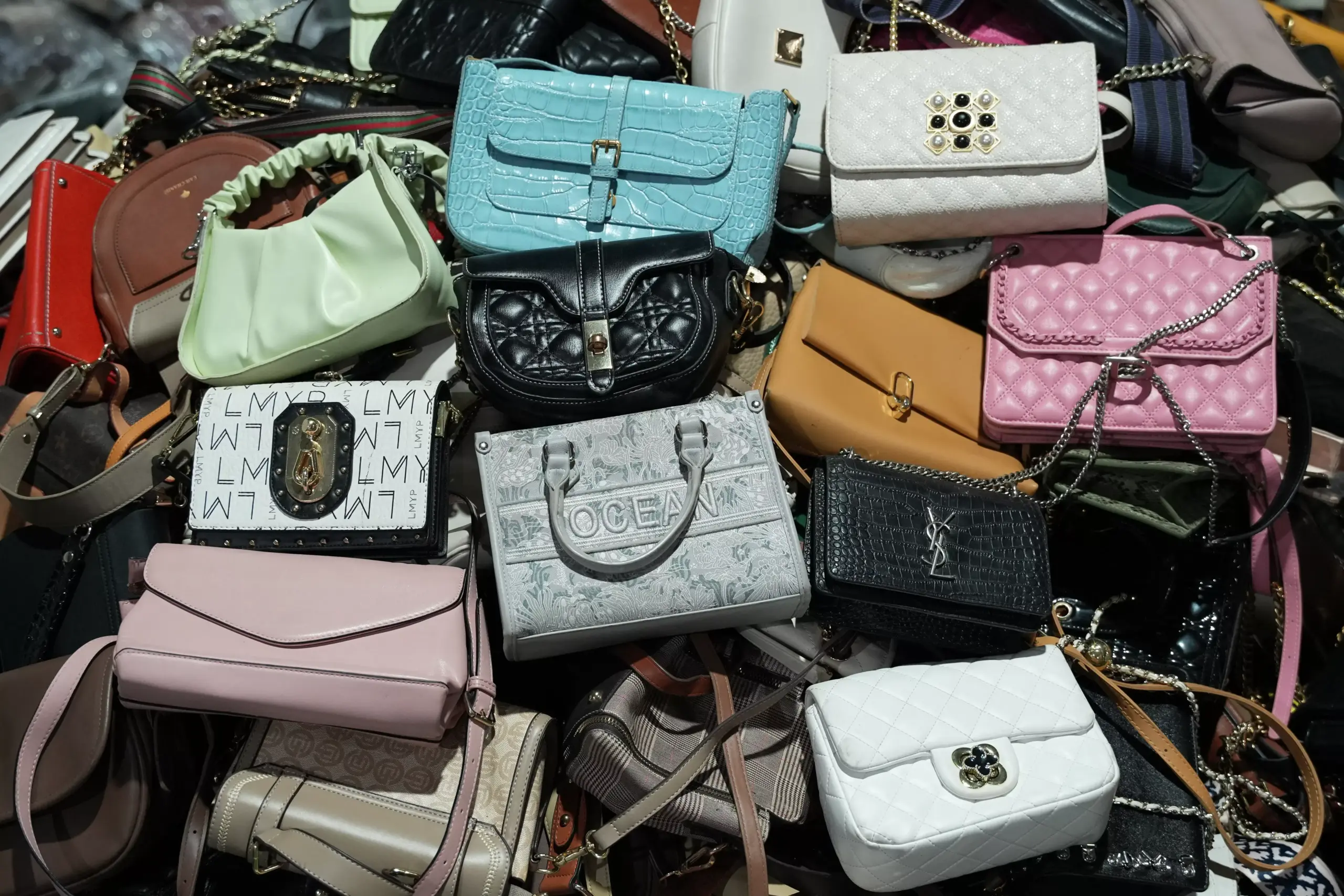 Quilted leather handbags in various colors and styles, including pink, blue, black, white, and beige, with different patterns and embellishments like chains and buckles.